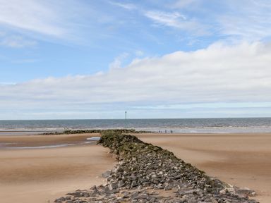 A sandy beach with a rocky jetty extending into the sea under a partly cloudy sky at Beeches Bach in Prestatyn
