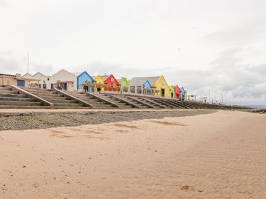A sandy beach with concrete steps leading up to a row of colorful buildings along the shoreline at Beeches Bach in Prestatyn