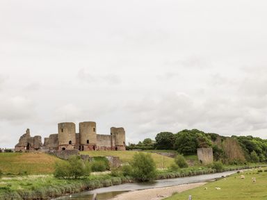 A landscape with castle ruins near a river and sheep grazing on grass at Beeches Bach in Prestatyn