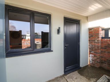 An entrance area with a dark door numbered 1 and a window next to it with brick walls at Chalet 5 in Sherburn