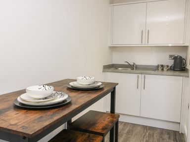 A kitchen with white cabinets and countertop a wooden table set with plates bowls and benches at Chalet 5 in Sherburn