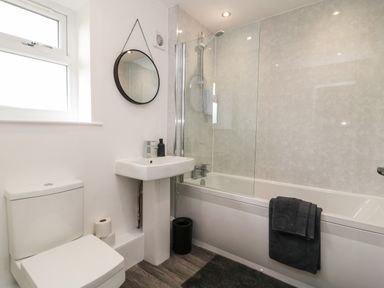 A bathroom with a toilet, pedestal sink with soap dispenser, bathtub with shower and glass screen and black towel at Chalet 5 in Sherburn