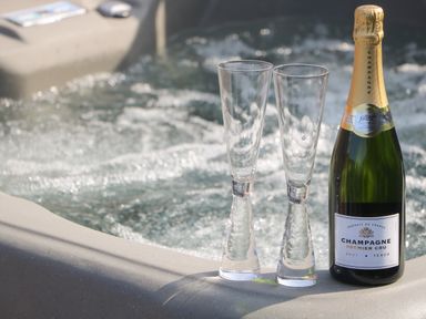 A bottle of champagne and two empty champagne glasses on the edge of a bubbling hot tub at Chalet 5 in Sherburn