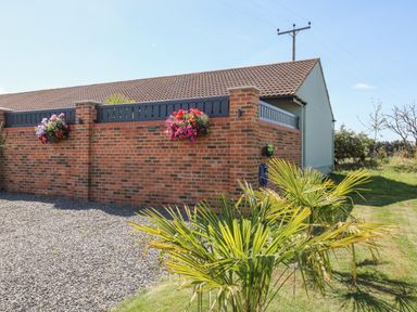 A brick wall with hanging flower baskets and a small building with a tiled roof behind it at Chalet 5 in Sherburn