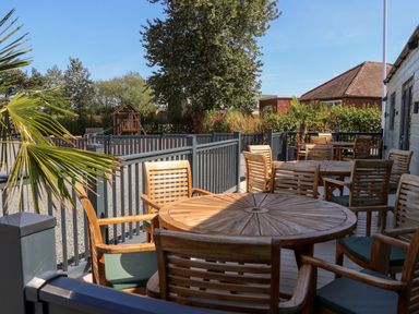 An outdoor seating area with wooden tables and chairs on a deck overlooking a playground at Chalet 5 in Sherburn