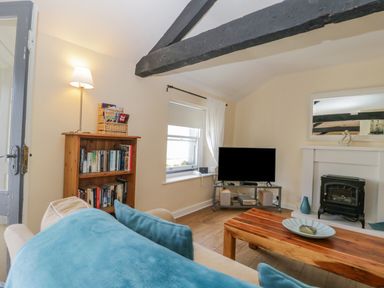 A living room with a wooden bookshelf a sofa with blue cushions a wooden coffee table a television and a fireplace at The Old Mill in Keswick
