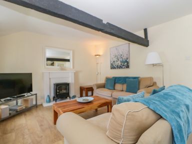 A living room with beige sofas and blue cushions a wooden coffee table a television and a fireplace at The Old Mill in Keswick