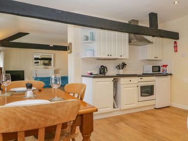 A kitchen and dining area with wooden table and chairs next to white cabinets and appliances at The Old Mill in Keswick