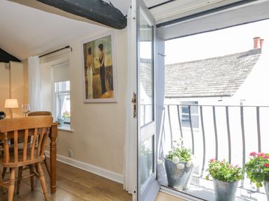 A dining area with wooden chairs and table next to a window and an open door leading to a balcony with flower pots at The Old Mill in Keswick