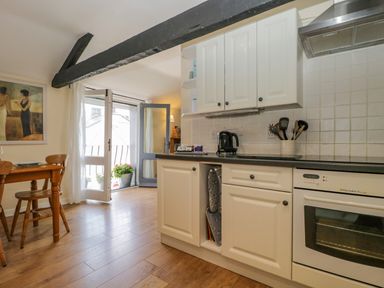 A kitchen with white cabinets a black countertop a kettle cooking utensils a dining table and chairs and a balcony door at The Old Mill in Keswick