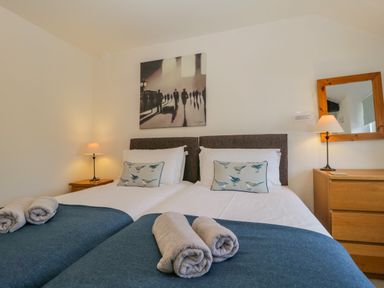 A bedroom with two single beds side by side with blue blankets and folded towels at the foot of the beds with a wooden dresser and mirror on the right and a bedside table with a lamp on the left at The Old Mill in Keswick