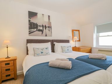 A bedroom with two single beds blue throws and rolled towels at The Old Mill in Keswick