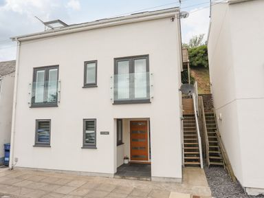 A modern white house with gray framed windows and a wooden door with stairs on the right at 3 Ty Stabal in Pwllheli
