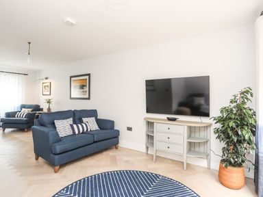 A living room with two blue sofas a wall-mounted TV and a potted plant at 3 Ty Stabal in Pwllheli