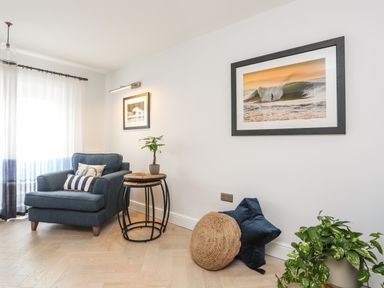 A seating area with a blue armchair next to nested round wooden and metal tables with a plant on top and framed pictures on white walls at 3 Ty Stabal in Pwllheli