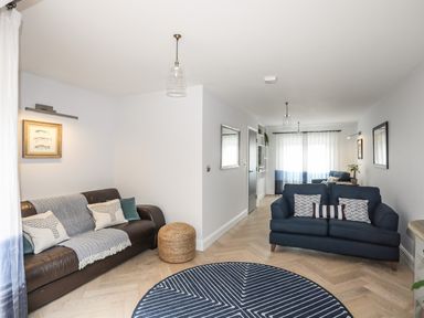 A living room with brown and blue sofas a round patterned rug and framed pictures on white walls at 3 Ty Stabal in Pwllheli