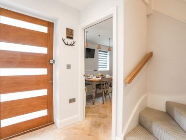 Entrance area with wooden front door next to carpeted stairs and open doorway to dining area at 3 Ty Stabal in Pwllheli
