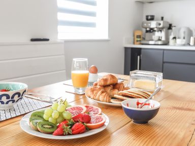 A wooden table with plates of fruit salad and pastries a glass of orange juice and a bowl with a spoon at 3 Ty Stabal in Pwllheli