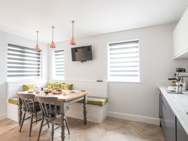 A kitchen with a corner dining bench, table set with breakfast items, three pendant lights, and a wall-mounted television at 3 Ty Stabal in Pwllheli