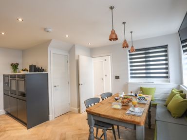 A kitchen dining area with a wooden table set for breakfast and green cushions on a bench at 3 Ty Stabal in Pwllheli