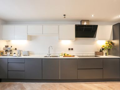 A modern kitchen with white upper cabinets dark lower cabinets a sink stove coffee machine and sunflowers on the counter at 3 Ty Stabal in Pwllheli