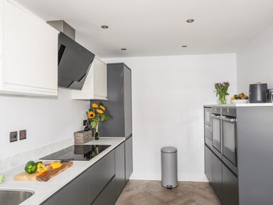 A kitchen with grey cabinets, black appliances, flowers on the counter, and a cutting board with peppers at 3 Ty Stabal in Pwllheli