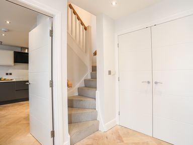 A hallway with carpeted stairs and white doors leading to a kitchen and a storage area at 3 Ty Stabal in Pwllheli
