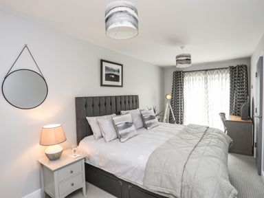 A bedroom with a large bed a bedside table with a lamp a round wall mirror curtains and a desk at 3 Ty Stabal in Pwllheli