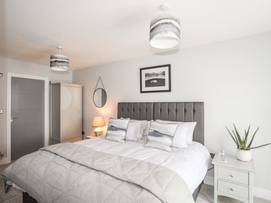 A bedroom with a large bed gray headboard nightstands with lamp and plant wardrobe and round mirror at 3 Ty Stabal in Pwllheli
