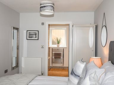 A bedroom with a bed pillows a wardrobe a mirror and a view into a bathroom with a towel rail and a plant on the windowsill at 3 Ty Stabal in Pwllheli