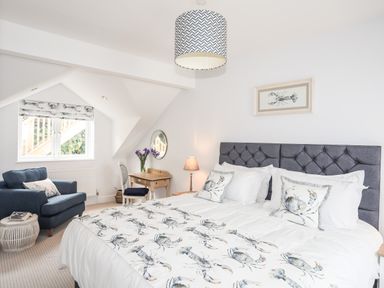 A bedroom with a double bed with crabs on bedding a blue armchair a wooden desk with a chair and a lamp at 3 Ty Stabal in Pwllheli