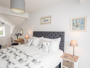 A bedroom with a bed with crab themed bedding and pillows two framed artworks two bedside tables with lamps and a wooden desk with a chair and flowers at 3 Ty Stabal in Pwllheli
