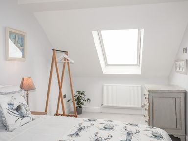 A bedroom with a bed a wooden clothes rack a radiator a chest of drawers and a skylight window at 3 Ty Stabal in Pwllheli
