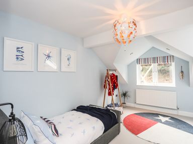 A bedroom with a single bed a round rug clothes rack and a window with a radiator at 3 Ty Stabal in Pwllheli