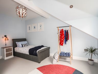 A bedroom with a single bed next to a nightstand lamp and framed pictures on wall at 3 Ty Stabal in Pwllheli