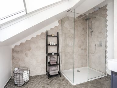 A bathroom with a corner shower enclosure glass shelves with towels and toiletries a wire basket with towels and a skylight at 3 Ty Stabal in Pwllheli