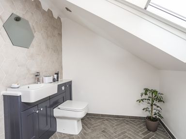 A bathroom with a wall-mounted sink and toilet under a sloped ceiling with a skylight and a potted plant on the tiled floor at 3 Ty Stabal in Pwllheli