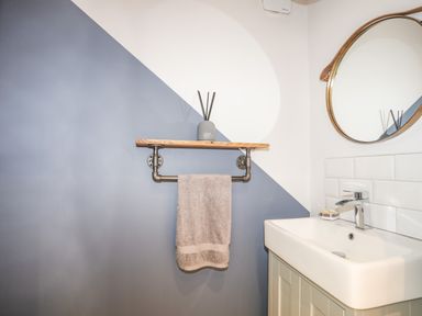 A bathroom sink with a faucet a round mirror and a towel hanging on a pipe towel rack at 3 Ty Stabal in Pwllheli