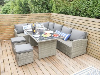 An outdoor patio with a wicker dining set including a glass top table a corner sofa with gray cushions two stools and food and drinks on the table at 3 Ty Stabal in Pwllheli