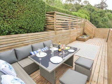 An outdoor seating area with a glass table a bottle and glasses on wooden decking at 3 Ty Stabal in Pwllheli