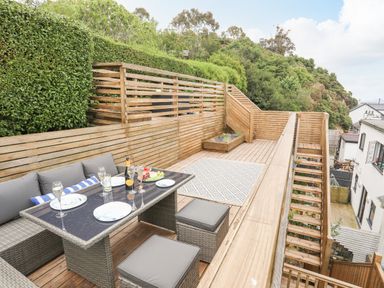 An outdoor wooden deck with a dining table set with plates and glasses at 3 Ty Stabal in Pwllheli