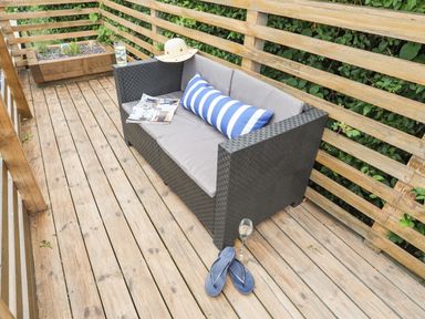 An outdoor wooden deck with a black wicker sofa with gray cushions and a striped pillow at 3 Ty Stabal in Pwllheli