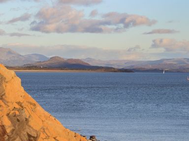 A body of water with rocky shore in foreground and hills and mountains in the background at 3 Ty Stabal in Pwllheli