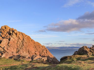 Rock formations beside a body of water with mountains in the background at 3 Ty Stabal in Pwllheli