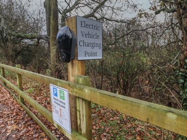 An electric vehicle charging point mounted on a wooden post beside a wooden fence in a wooded area