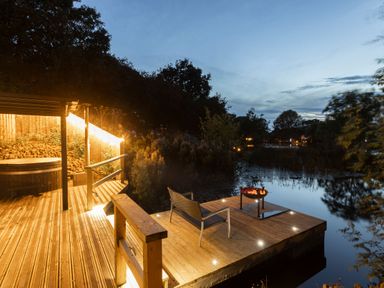 A wooden deck with a chair and fire pit next to a pond at The Shepherds Hut at Bridge Lake Farm & Fishery in Chacombe