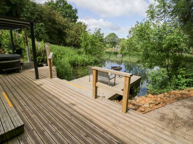 A deck overlooking a pond with seating at The Shepherds Hut at Bridge Lake Farm & Fishery Chacombe