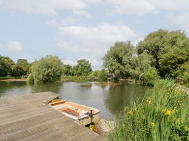 A lake with a boat on a dock at The Shepherds Hut at Bridge Lake Farm & Fishery Chacombe