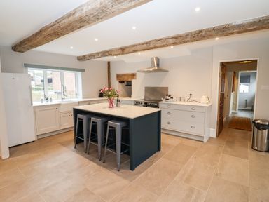 A kitchen with a central island and three stools under wooden ceiling beams at Ley Mill Farm in Huntley