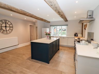 A kitchen with a central island, large wall clock, exposed wooden beams, and a window at Ley Mill Farm in Huntley